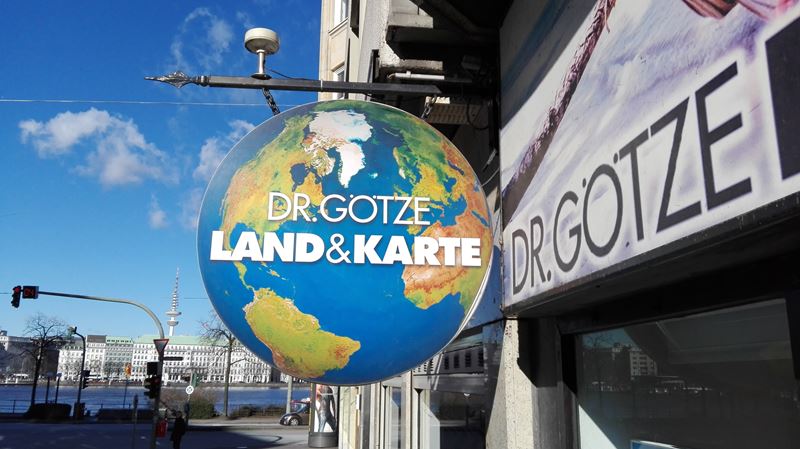 Ladenschild in Form der Erdkugel mit Beschriftung »Dr. Götze Land & Karte«.