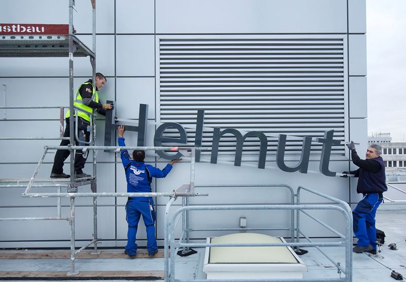 Drei Handwerker bringen einen Teil des Schriftzugs »Hamburg Airport – Helmut Schmidt« an.