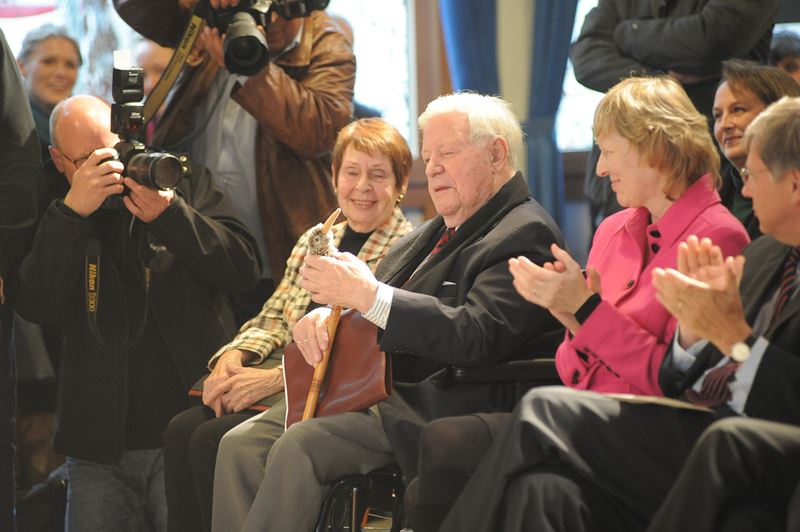 Helmut Schmidt und seine Partnerin Ruth Loah lächeln. Er hält den Plüschkiwi, das Maskottchen des Helmut-Schmidt-Gymnasiums, in den Händen.
